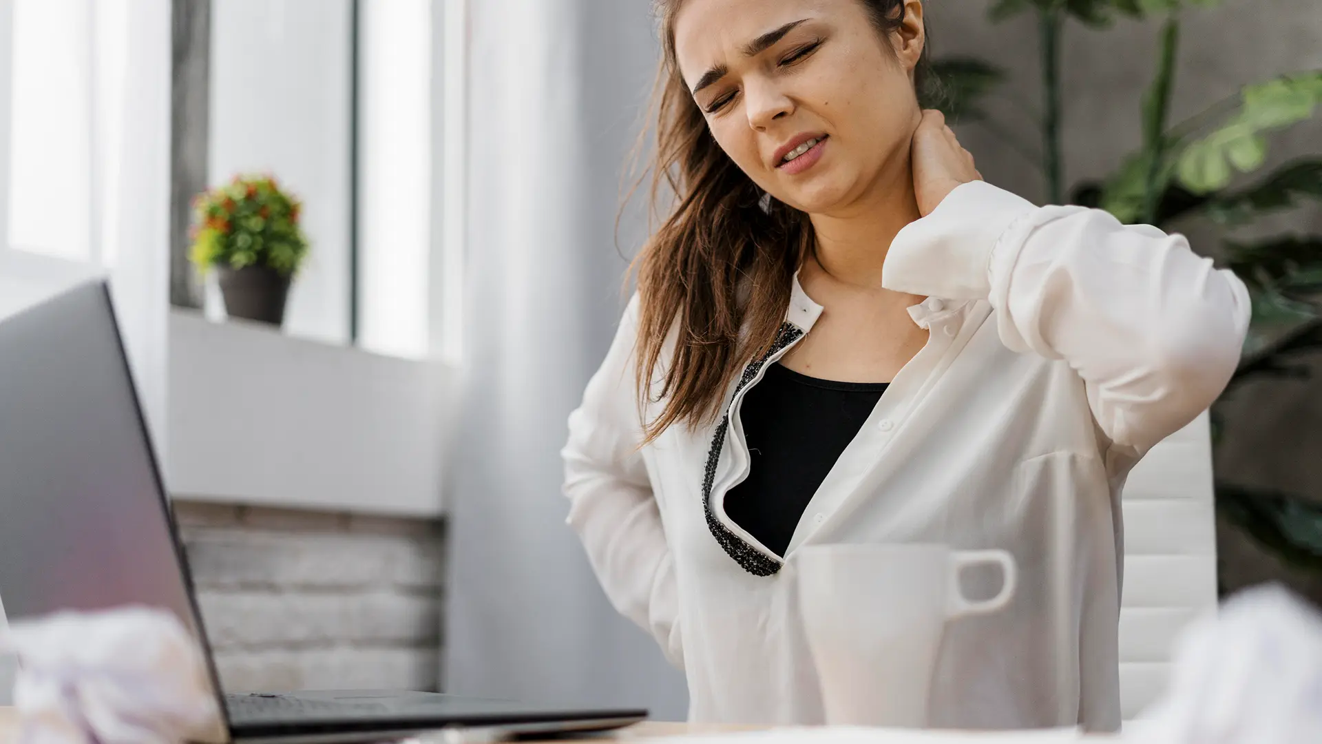 Mulher sentada em frente ao computador sentindo dor na coluna